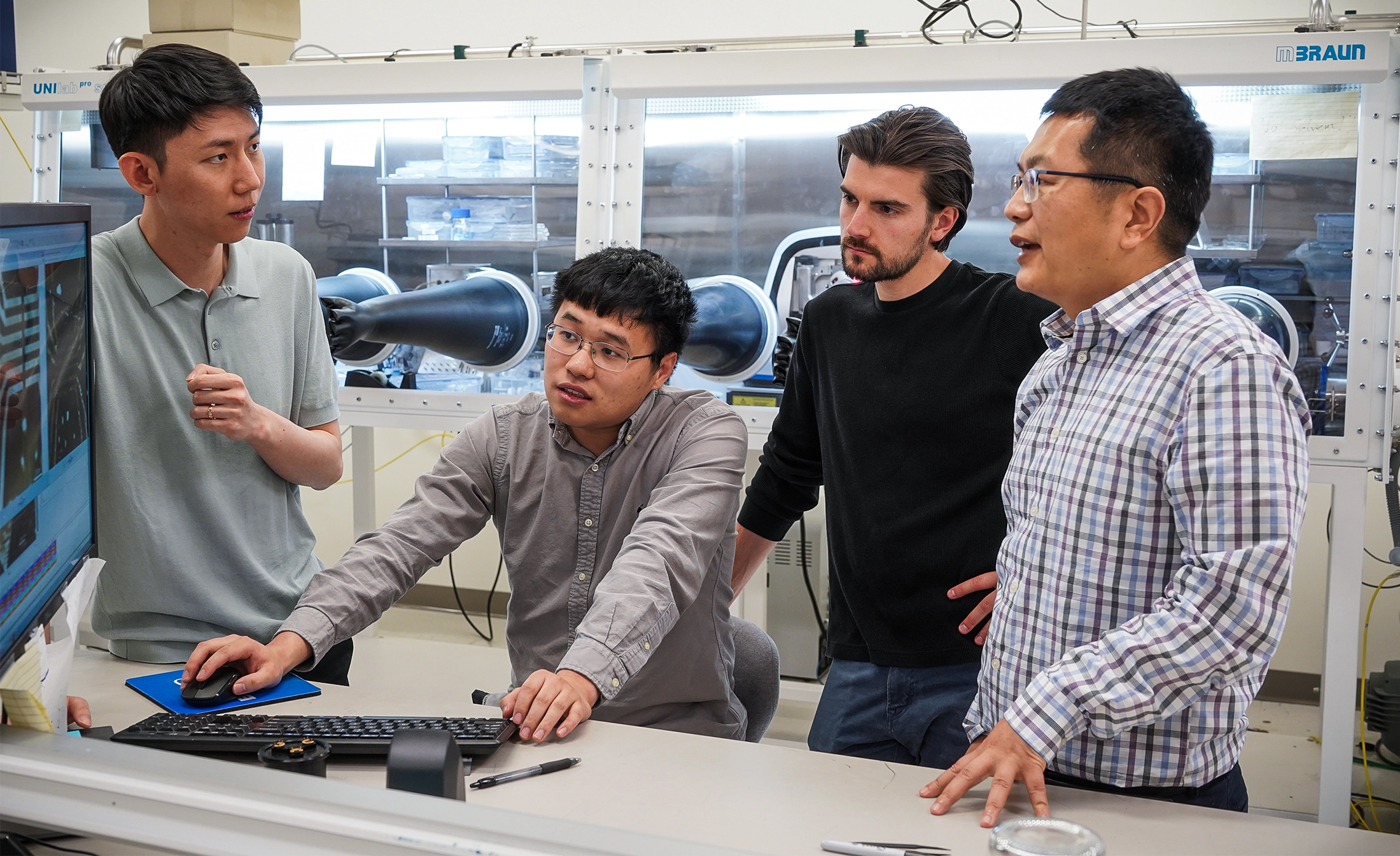 Xiaodong Xu (right) speaking to three other students in a lab.